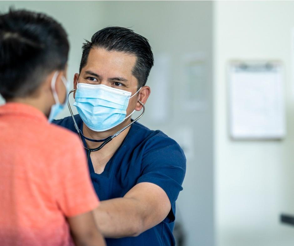 Masked medical professional listening to boy's chest